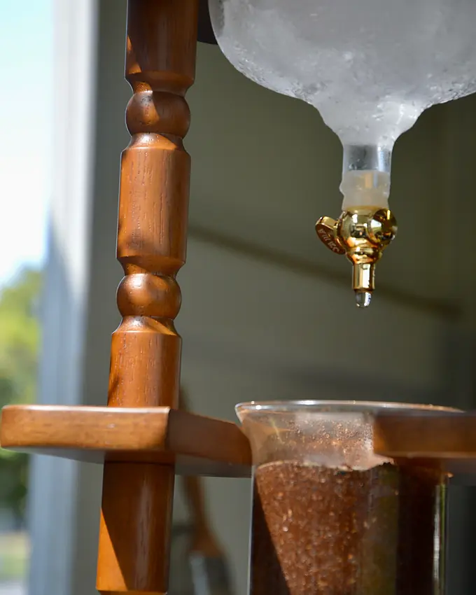 The cold drip tower: frosted glass, a brass tap and coffee grounds in a timber stand
