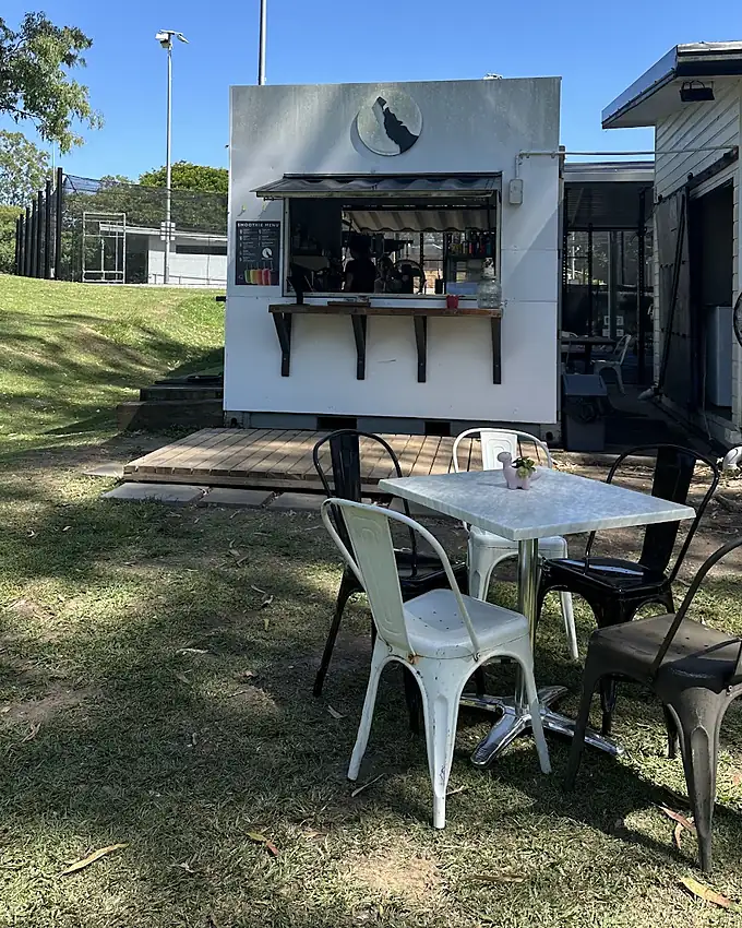 A marble table and metal chairs on the grass in front of the coffee window and its timber deck