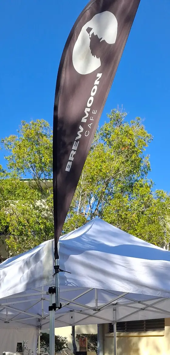 The Brew Moon Cafe flag, with the moon and the wolf on it, flying over the white gazebo at a market