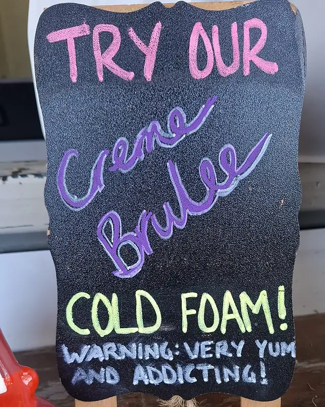 A chalkboard that reads Try our creme brulee cold foam, warning, very yum and addicting